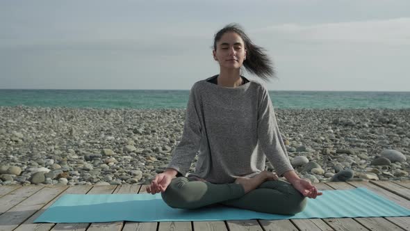 Brunette Is Sitting with Closed Eyes on Floor Outdoors in Seascape Background