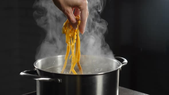 Female Chef Putting Raw Pasta Into Boiling Water, White Smoke in Slow Motion Rising Above Hot