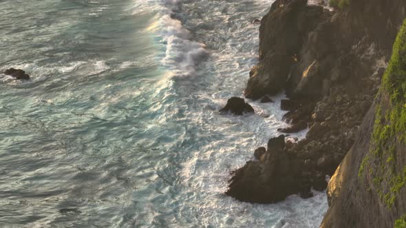 Large waves crashing on rocky tropical island shore, turbulent surface, white foam