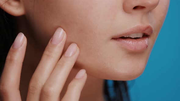 Close-up of Woman Applying Moisturizer on Her Cheek and Chin on Blue Background