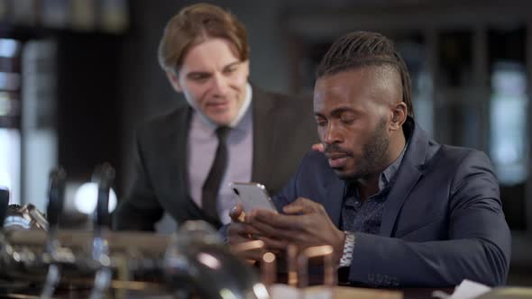 Handsome Positive African American Man in Suit Texting on Smartphone Greeting Caucasian Colleague