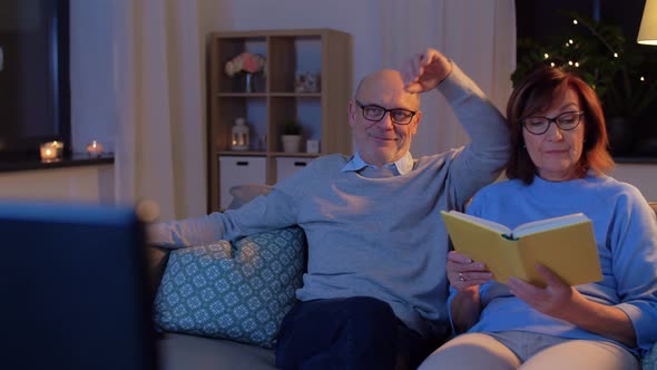 Senior Couple Watching Tv and Reading Book at Home