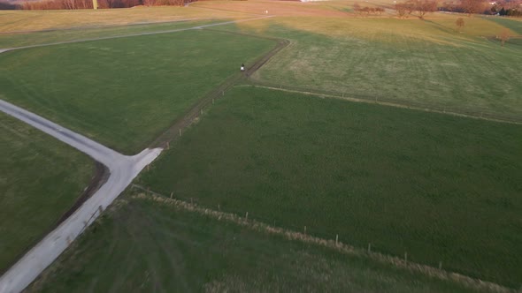 Person sitting on his white scooter in a lush field during sunset. Wide angle aerial tracking shot r