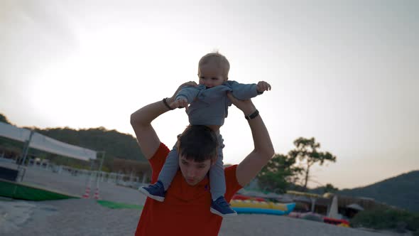 Father Entertains Little Son Carrying on Shoulders on Beach