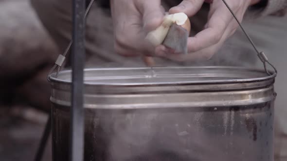 Tourist Slices a Mushroom with Knife Into Camping Pot. Man Prepares Mushroom Soup on Camp Black