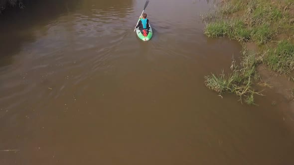Man kayaking on meandering river, drone closely follows and pans up to reveal beautiful landscape