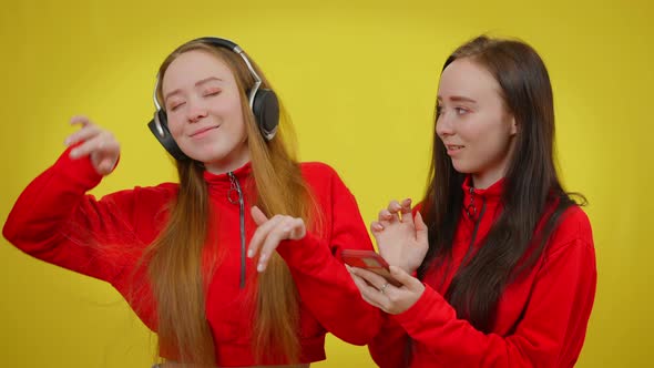 Happy Woman in Headphones Dancing As Twin Sister Changing Music on Smartphone