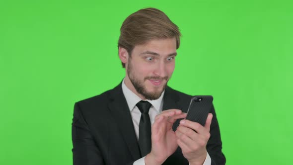 Young Businessman Celebrating on Smartphone on Green Background