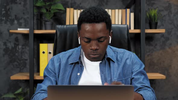 African American Man Inserts Wireless Earphones Into Ears Works for Laptop