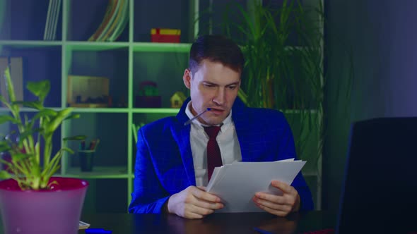 Young Man Holds Pen in Mouth and Examines Documents Sitting in Office