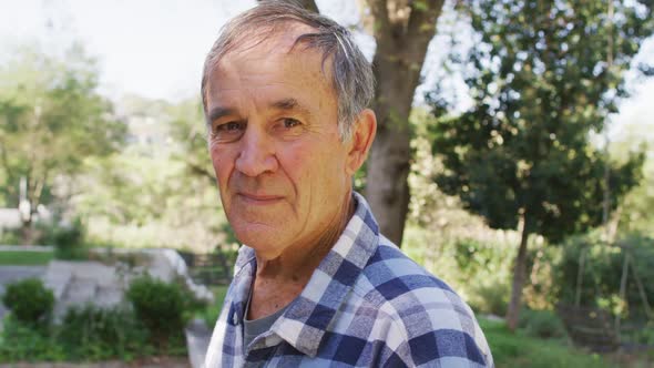 Portrait of smiling caucasian senior man looking at camera outdoors in garden