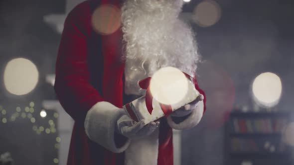 Sant Claus Holding and Shaking Wrapped Giftbox in Decorated Room