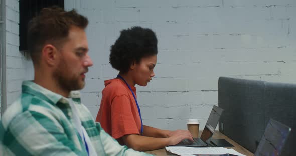 A Man and Woman Work at Laptops Sitting at One Work Desk in a Office