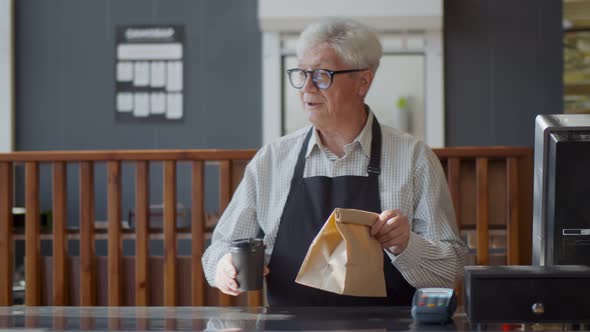 Senior Waiter at Counter Giving Paper Bag and Coffee Cup with Take Away Order in Cafe