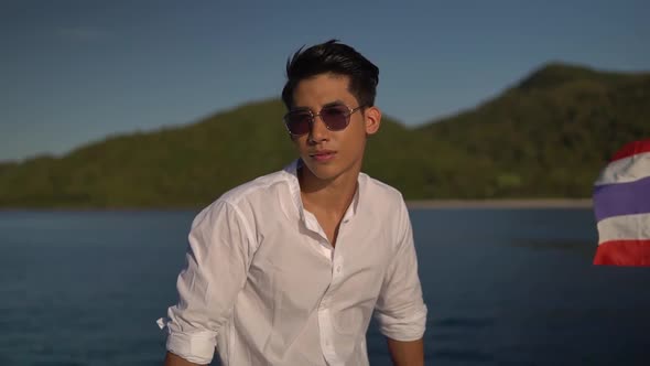 Stylish Young Man in White Shirt Posing on Yacht Board Wearing Sunglasses Smiling and Enjoying a