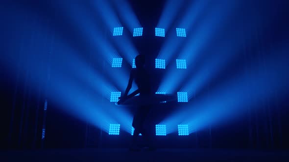 Graceful Silhouette Ballerina Doing a Workout in the Classroom. Smoke in the Rays of Blue Light