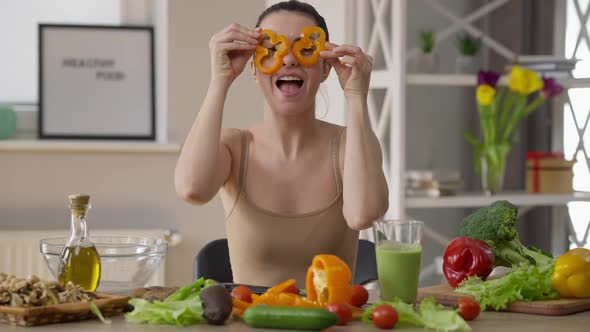 Joyful Carefree Vegan Woman Having Fun Putting Bell Pepper Circles on Eyes Laughing