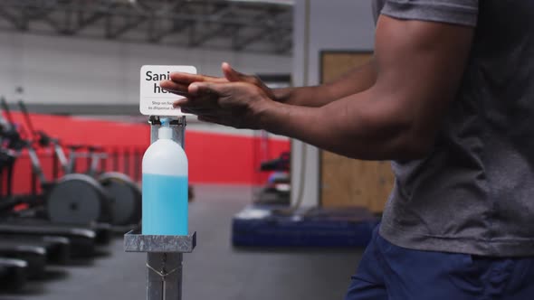 Mid section of fit african american man sanitizing his hands in the gym