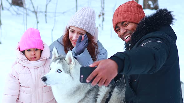 Afro Man with His Caucasian Wife Having Fun with a Beautiful Daughter Playing Husky in Snowy Park