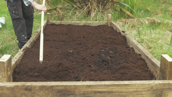 Young man using raking leveling compost soil in raised garden bed