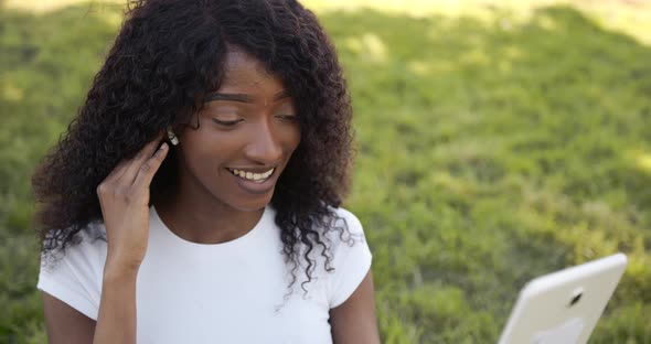 Joyful Black Woman Listening to Music on Tablet in Park in Sunny Day