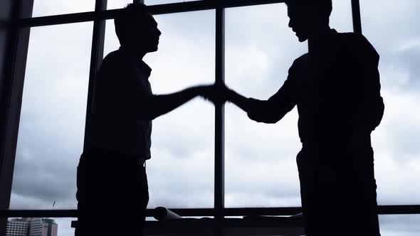 Silhouettes of two businessman shaking hands in the office.