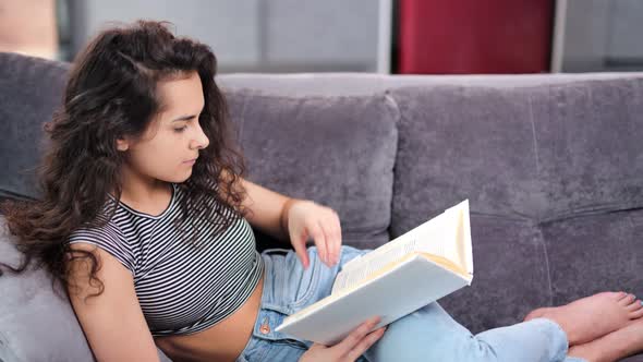 Confident Mixed Race Woman Reader Resting on Couch Reading Interesting Book Medium Shot