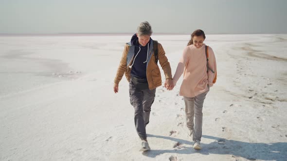 Happy Lovely Couple Travelers Walking Hand to Hand on Pink White Salty Coast