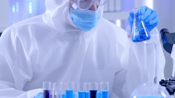Scientist in PPE suite doing some research checking a liquid in a test tube at laboratory.