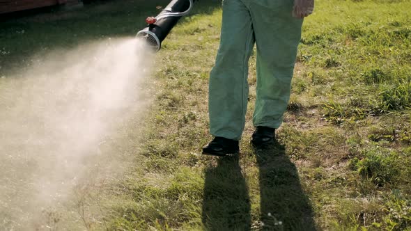 Farmer in Protective Clothes Spray Pesticides. Farm Worker Spray Pesticide Insecticide on Green