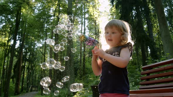 Kid Blows Bubbles From Special Manual Bubble Machine Outdoors in Park