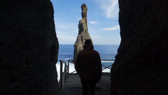 Young man walking out of dark cave towards the ocean