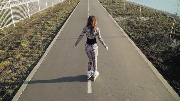 Athletic slender girl rollerblading on the path along the lake. Slow motion.