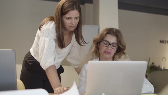 Female Professionals Sitting and Standing at Table with Laptop