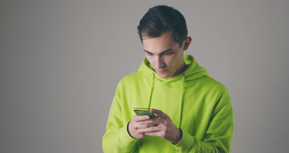 Young Handsome Man in a Bright Sweater Using Smartphone on Grey Studio Background