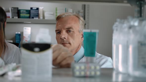 An Adult Man Pharmacist Audits the Product in the Interior of a Modern Pharmacy