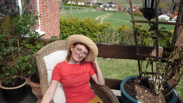 Smiling redheaded woman wearing straw hat sitting on balcony