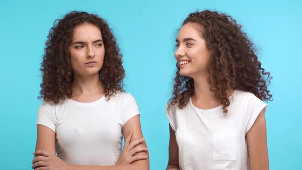 Two Beautiful Young Curly Female Twins Touching Each Other Hair Smiling on Blue Background