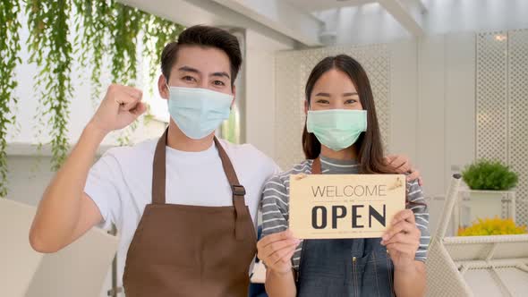 Business owner attractive young Asian couple in apron hanging we're open sign