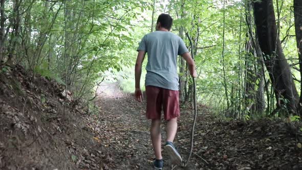 A man walks on a footpath in forest, daytime,  summer season. Young man filmed from behind while Wal