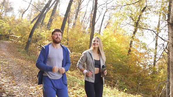 Married Couple Dressed in Sports Clothes Running Around the Park on a Sunny Autumn Day Surrounded By