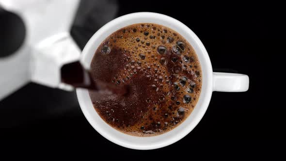 pour black coffee in white cup on black background, top view. 4K UHD video
