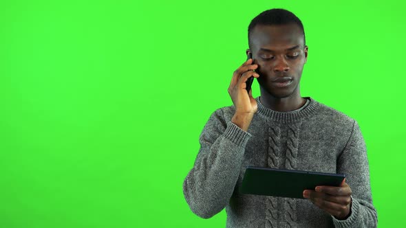 A Young Black Man Talks on a Smartphone While Holding a Tablet - Green Screen Studio