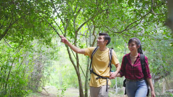 Asian couple are feeling fresh and relax in nature wild, looking and pointing the view in forest