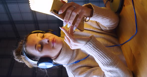 A 30Yearold Woman in Headphones Listening to the Music and Online Messaging Via Smartphone