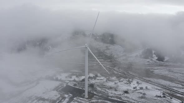 Wind turbine in a snowy landscape with early winter morning mist.