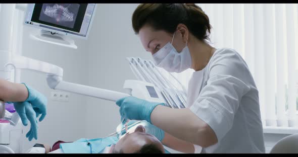 A Female Dentist Examines the Oral Cavity of a Patient Lying on a Dental Chair