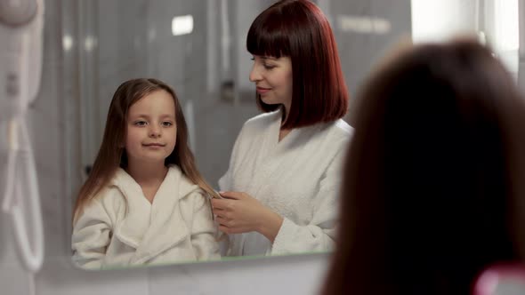 Loving Mom Brushing Hair of Cute Little Girl in the Bathroom