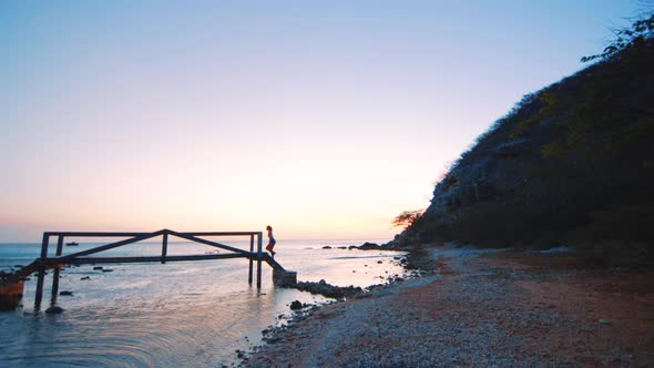 Young girl walking over wodden bridge during sunset in the background