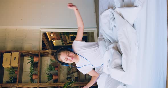 10 Years Old Girl Sits on a Bed in Headphones and Listening to Music Via Smartphone App